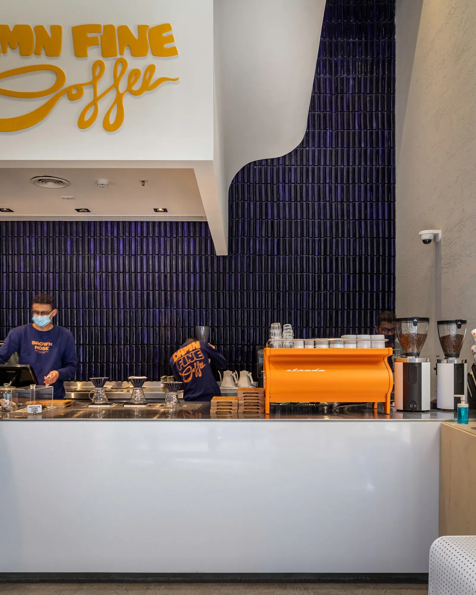 Barista behind the white counter in front of the blue tile wall